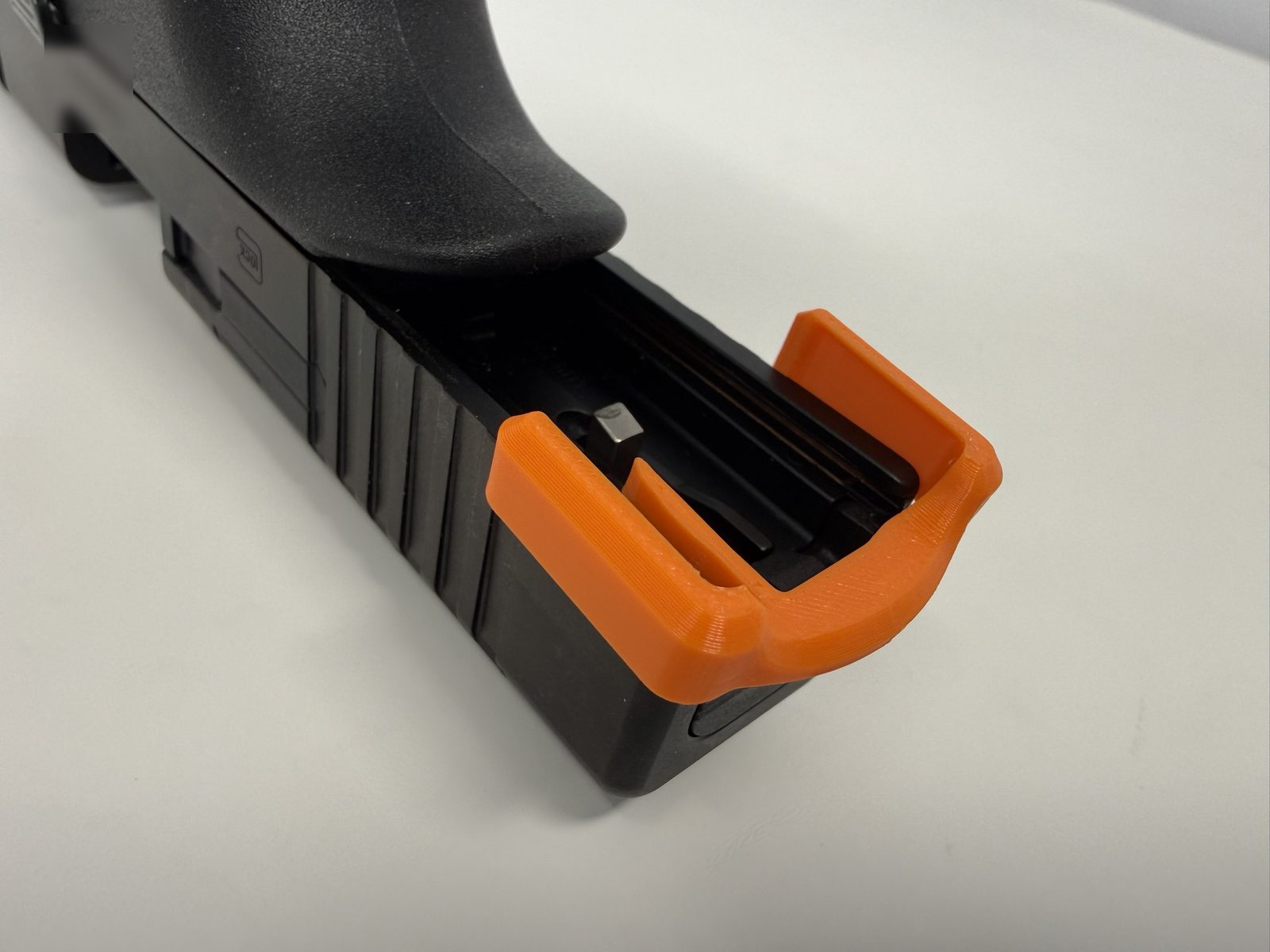 Angled view from underneath the rear of a Glock slide with an orange ResetClip partly on, its side arms lined up with the grooves at the rear of the slide.