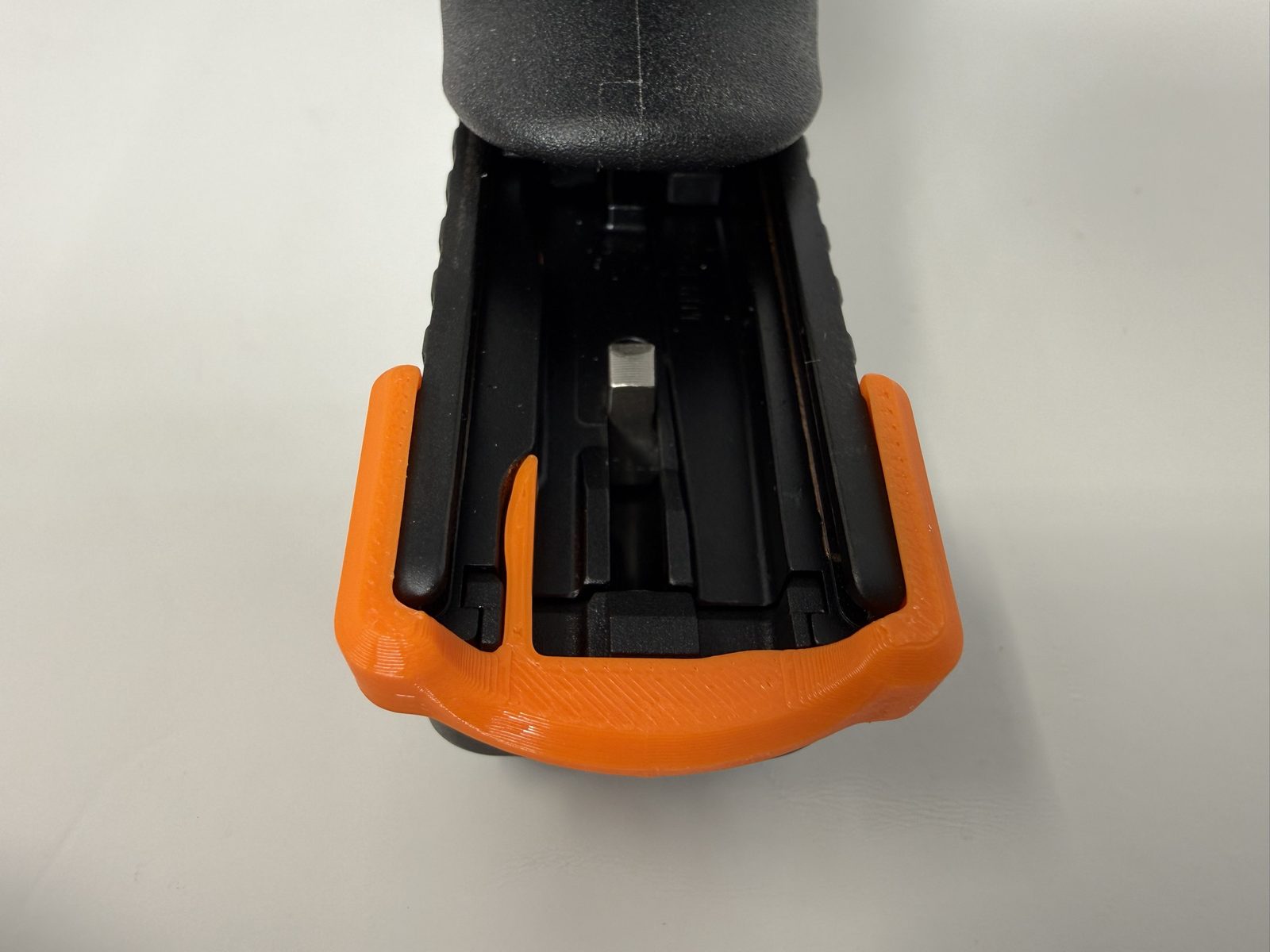 View from underneath the rear of a Glock slide showing an orange ResetClip fully seated, the U wrapped around the slide and the thin centre blade inside.