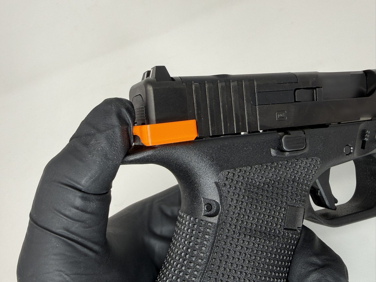 Close-up of an orange ResetClip fully seated over the rear of a Glock slide, held in a gloved hand.