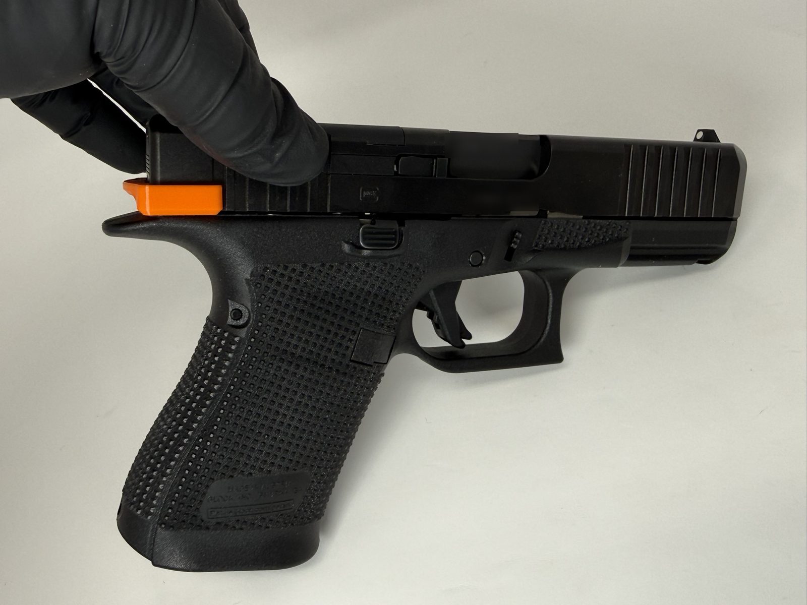 Left side of a Glock pistol with an orange ResetClip fully seated over the rear of the slide.